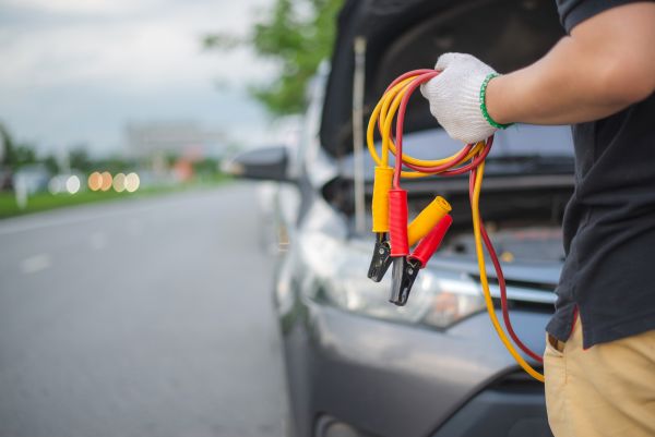 Person holding jumper cables in front of car with open hood on roadside in Sun City – Pete Nelson Automotive battery service